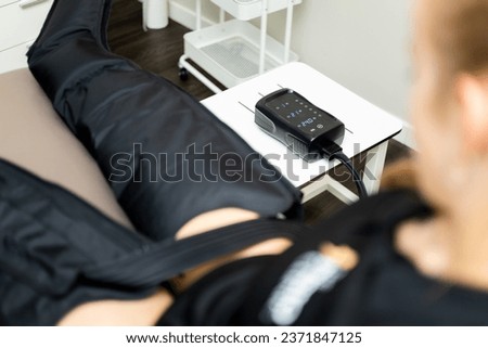 An unrecognizable woman visits a physiotherapy clinic to undergo a body pressotherapy session through a pneumatic suit for benefits in the circulatory and lymphatic system. Royalty-Free Stock Photo #2371847125