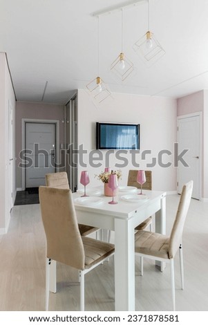 A modern living room combined with a kitchen, in light colors. Dining table with pink tableware.