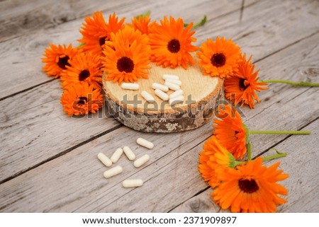 Calendula alternative medicine. White pills on a wooden table, fresh blooming calendula background,
