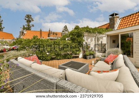an outdoor living area with couches and flowers in the foreground, taken from above it is a blue sky filled with white