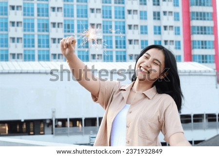 happy asian young woman holding sparklers celebrate new year eve in outdoor roof top with city building background