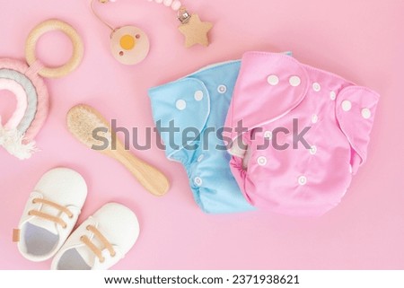 Flat lay with reusable cloth baby diaper, toys and accessories. Eco friendly nappy on pink pastel background. Sustainable lifestyle, zero waste idea