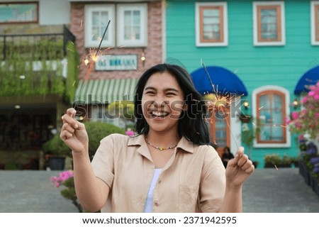 cheerful young asian woman holding sparkler to celebrate new year eve with garden party standing over colorful vintage house yard