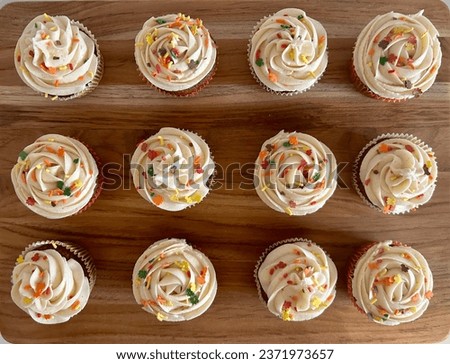 Top down photo of a dozen cupcakes with swirled icing and fall themed sprinkles on a light wood background.