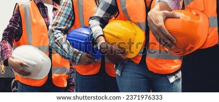 Full team engineers men and women workers of various nationalities wearing vests standing in line holding safety helmets to ensure safety and prevent accidents while working in the factory industry.