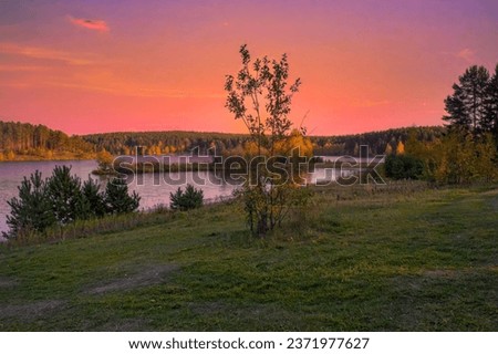 Autumn landscape with riverbank at sunset. Wonderful nature, beautiful natural background. Sky with clouds is reflected in the water.