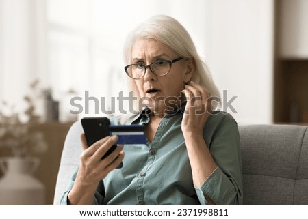 Worried surprised elderly woman in glasses looking at smartphone and credit card, getting financial problems, bad online bank service, finding overspending, bankruptcy risk Royalty-Free Stock Photo #2371998811