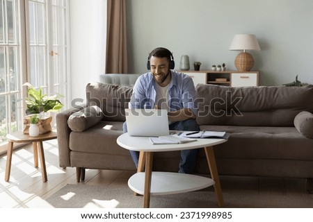 Happy positive millennial freelance employee man in wireless headphones talking on video call at laptop, laughing, smiling, enjoying online conversation, Internet communication, studying from home