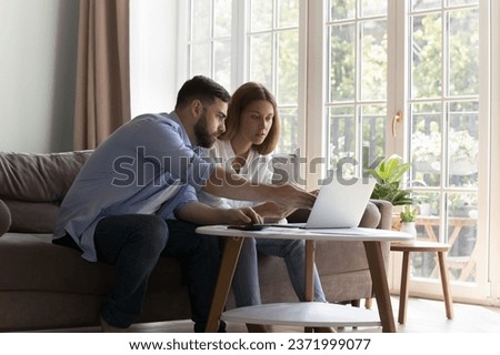 Concerned serious family couple talking, discussing expenses, budget overspending, online payment app error, looking, pointing at laptop display, checking financial reports, using calculator Royalty-Free Stock Photo #2371999077
