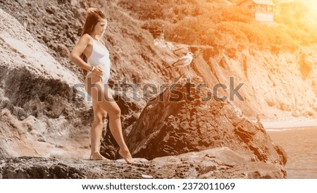 Woman travel sea. Happy tourist in white bikini enjoy taking picture outdoors for memories. Woman traveler posing on the beach at sea surrounded by volcanic mountains, sharing travel adventure journey