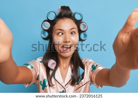 Cute girl in pajamas and curlers fools around with her phone making funny faces, morning mood concept, copy space