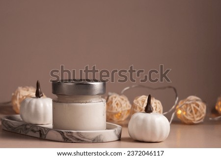 Aromatic candle on marble tray with pumpkins and warm lights on a beige background, copy space