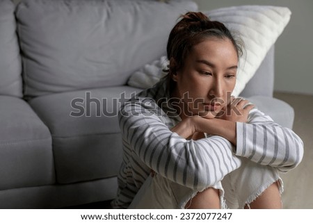 Lonely Asian woman in distress, worried, confused, sitting on floor at home. Female suffer from mental health problems.