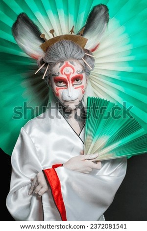 Attractive woman with green fan. Halloween model with makeup and rabbit mask, closeup portrait