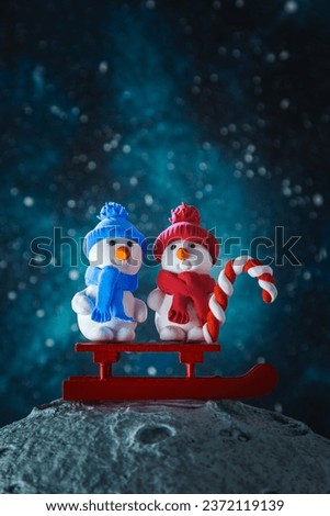 Two cute plasticine snowmen with a sled and a lollipop on the moon. Christmas card.