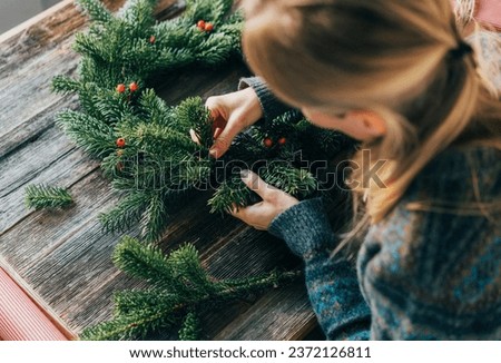 An unrecognizable woman makes a spruce festive wreath and decorates it. Royalty-Free Stock Photo #2372126811