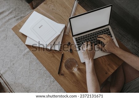 Aesthetic minimalist home office workspace desk. Person working on laptop computer. Notebook, glass of water, stationery. Blank mockup screen template. Flat lay, top view work, business concept