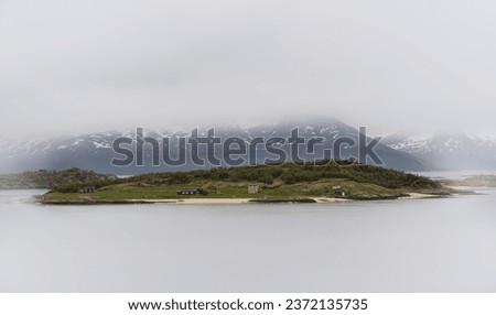Serene norwegian island: distant drone view captures panoramic misty landscape of a siland surouned by clouds. Panoramic shot from above. Calm waters on a early summer morning. Royalty-Free Stock Photo #2372135735