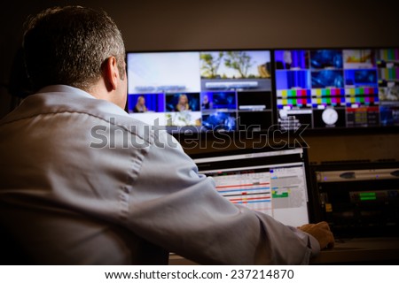 TV director at editor in studio. TV director talking to vision mixer in a television broadcast gallery.Man sat at a vision mixing panel in a television studio gallery Royalty-Free Stock Photo #237214870