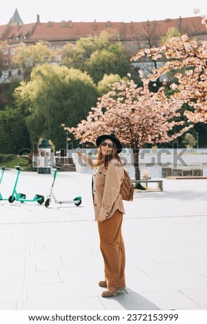 Attractive young female tourist is exploring new city. Redhead 30s girl in black hat and sunglasses resting near Wawel castle, Cracow, Poland. Traveling Europe in spring. High quality photo, full body