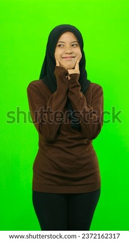 A beautiful girl wearing a black hijab and a brown sweater is expressing happiness