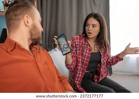 Conflicts, quarrels, jealousy in a young family. Angry woman is jealous and screams, found about mistress, takes her husband phone. Copy space Royalty-Free Stock Photo #2372177177
