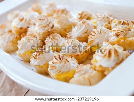 Mini Lemon Meringue Pies Tarts in white porcelain serving tray. Shot with narrow depth of field, bokeh effect. Focus on foreground. Food photography.