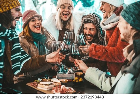 Happy friends group toasting red wine dining at restaurant terrace - Young people socializing drinking and eating food sitting outside at winery bar table - Winter season - Dinner lifestyle concept