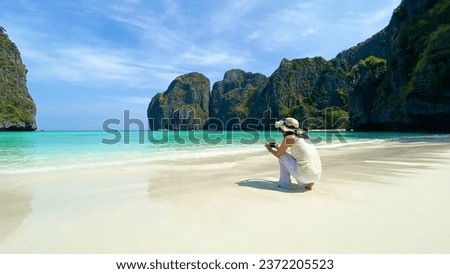 Young Asian woman hands holding mobile smart phone taking photo of  beautiful sea beach view at Maya bay Krabi Thailand.