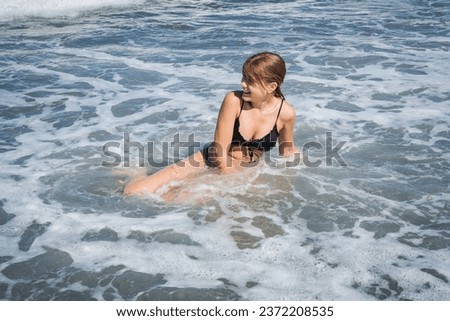 Happy emotional teenage girl swims in foamy stormy sea waves on a sunny warm summer day. The concept of a long-awaited vacation and traveling with children
