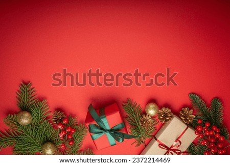 Christmas or New Year celebration red paper festive background with decoration fir tree, wrapped present boxes, cones, berries, sparkly red balls. Space for text.