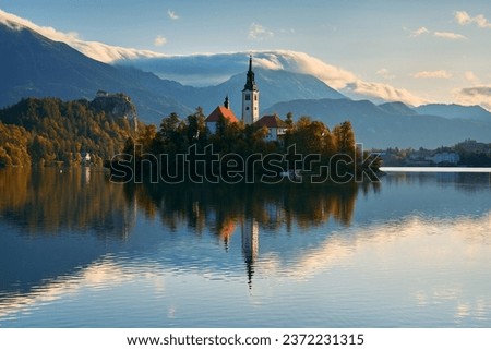 A calm autumn morning on Lake Bled. An island with a church in the foreground and a castle and mountains in the background. Royalty-Free Stock Photo #2372231315