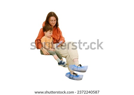 A patient and her baby sit in the clinic corridor, watching videos on their phone while waiting for their turn to see the doctor, isolated on white background. Kid boy aged two years (two-year-old)