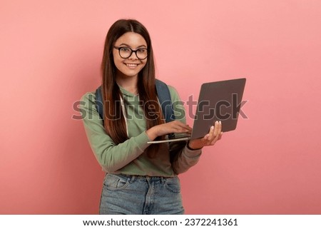 Happy Teen Student Girl Holding Laptop And Smiling At Camera, Nerdy Female Teenager Using Computer For Online Study And Distance Learning, Posing Over Pink Studio Background, Copy Space