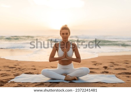 Sunset meditation. Calm lady meditating outdoors on sea beach, sitting on fitness mat and keeping hands in namaste gesture, practicing yoga outside