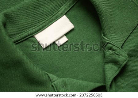 Blank white laundry care clothes label on green shirt fabric texture background