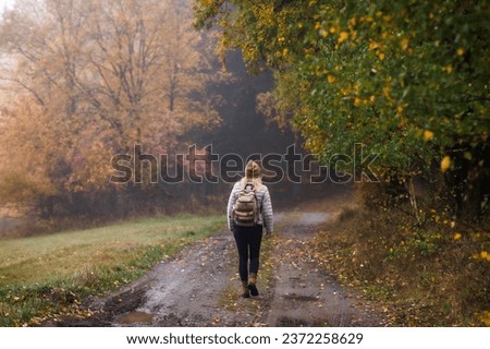 Solo travel and eco tourism. Woman hiking on footpath in autumn forest. Fog weather Royalty-Free Stock Photo #2372258629