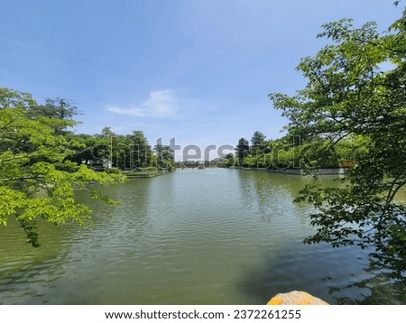 Historical landmarks, Kuwana city, Japan, park with lakes, many trees, symbols and sculpture, blue sky, orange bridge.