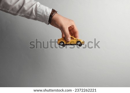Man's hand in white shirt holds toy taxi car on gray background