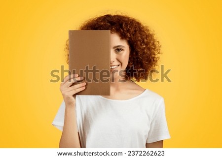 Happy pretty european teen woman hold book, has fun, enjoy spare time, isolated on yellow background, studio, close up. Study, education, planning day and diary, ad and offer Royalty-Free Stock Photo #2372262623