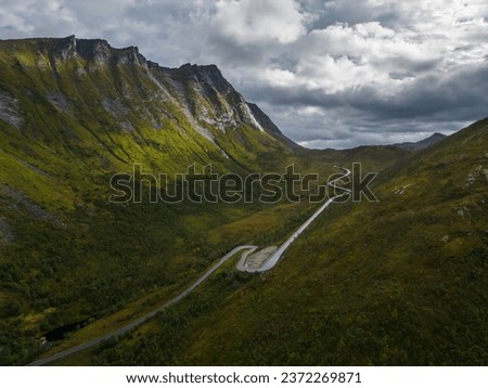 A curved road in a beautiful mountain valley. Sunlight on the mountain side. Dramatic clouds on the sky. High angle view.
