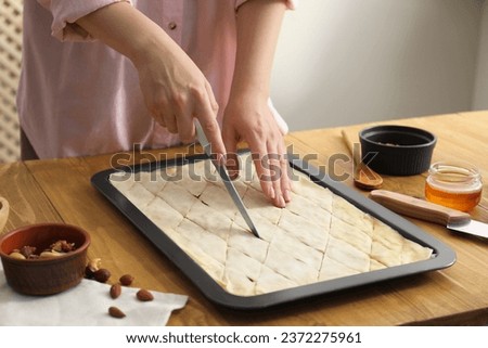 Making delicious baklava. Woman cutting dough in baking pan at wooden table, closeup Royalty-Free Stock Photo #2372275961