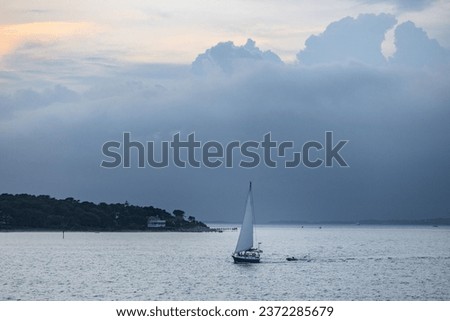A scenic view of a boat sailing off the coast of cape cod at sunset under a bright stormy sky