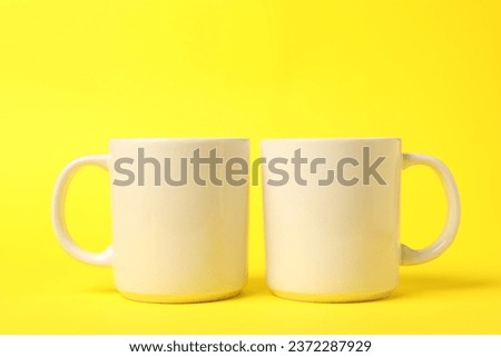 Two white ceramic mugs on yellow background