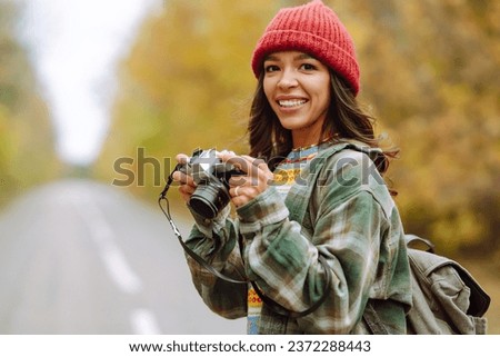 Woman tourist with a retro camera and backpack on a hike in a yellow autumn forest. Young woman walking and having fun outdoors.