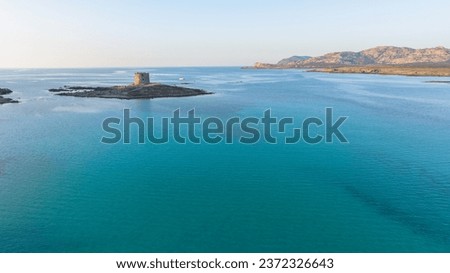 Aerial photo of the old prison tower on Isola Della Pelosa in the northwest of Sardinia in the Province of Sassari. Stintino town, Sardinia, Italy. Sunny day, blue sky, clear water.