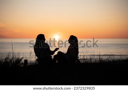 Silhouette of two female friends enjoying a conversation while sitting and watching the sunset on a sea beach. Back view Royalty-Free Stock Photo #2372329835