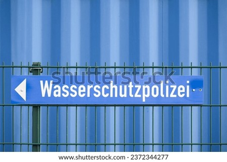 Sign with the German word Wasserschutzpolizei meaning water protection police on a fence in front of a blue wall, copy space, selected focus