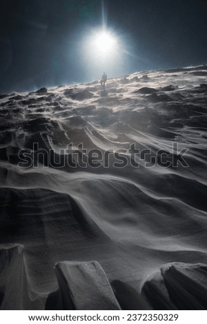 A lone hiker in warm clothes, in the cold winter walks on the frozen mountain, on sunny day with clear blue sky and strong wind