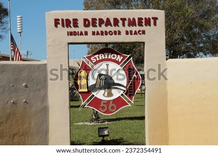 fire department indian harbour beach fire station department sign logo on grass next to bushes with palm trees and sky above, close up